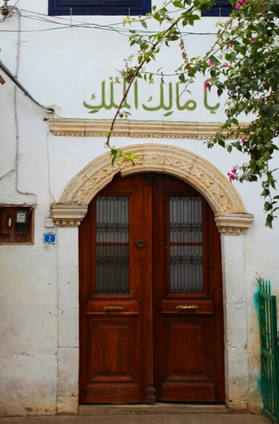 A carved wooden door beneath the words Ya Malik al-Mulk